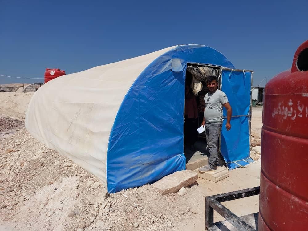 Ein Mann steht vor einem blau-weißen Zelt.