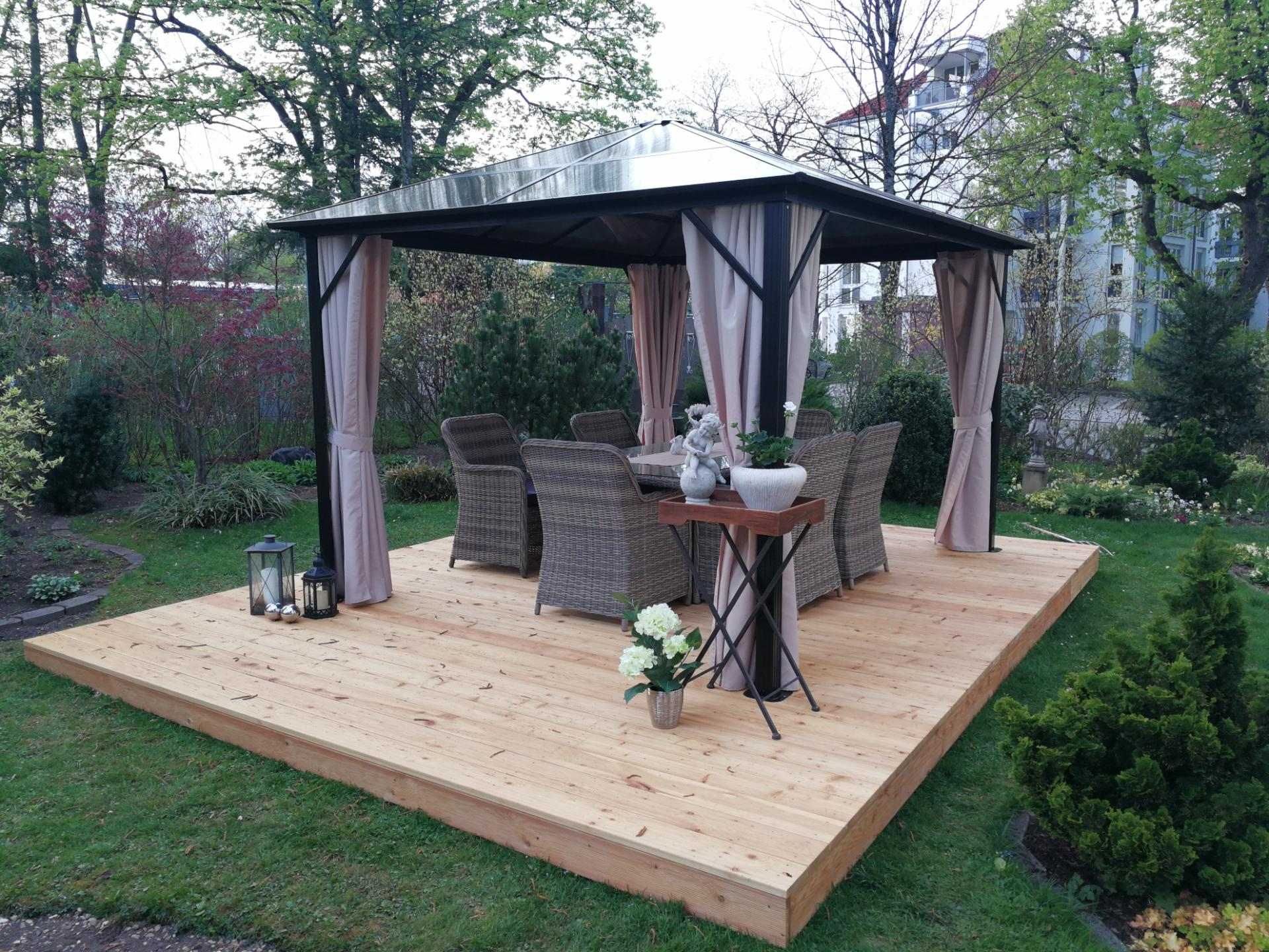 Gartenpavillon mit Holzboden und Essgruppe, umgeben von Rasen und Pflanzen.