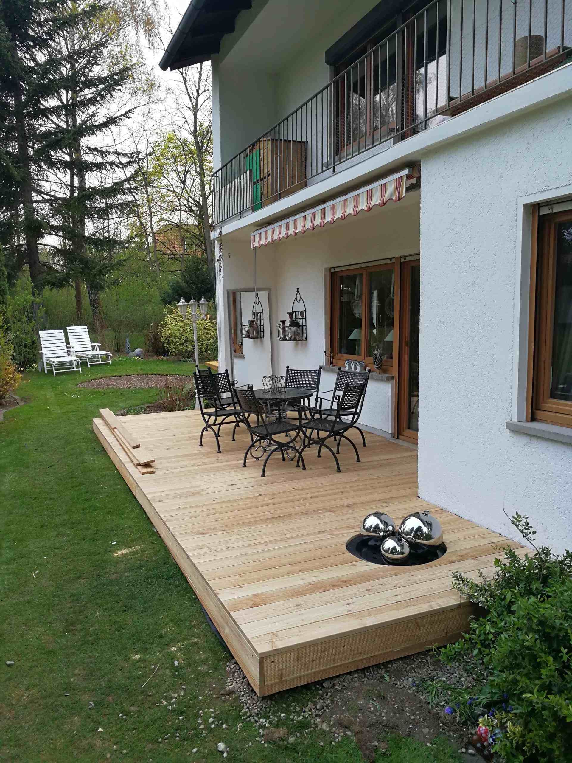 Terrasse mit Holzboden und Gartentischgarnitur vor einem Haus mit Garten.