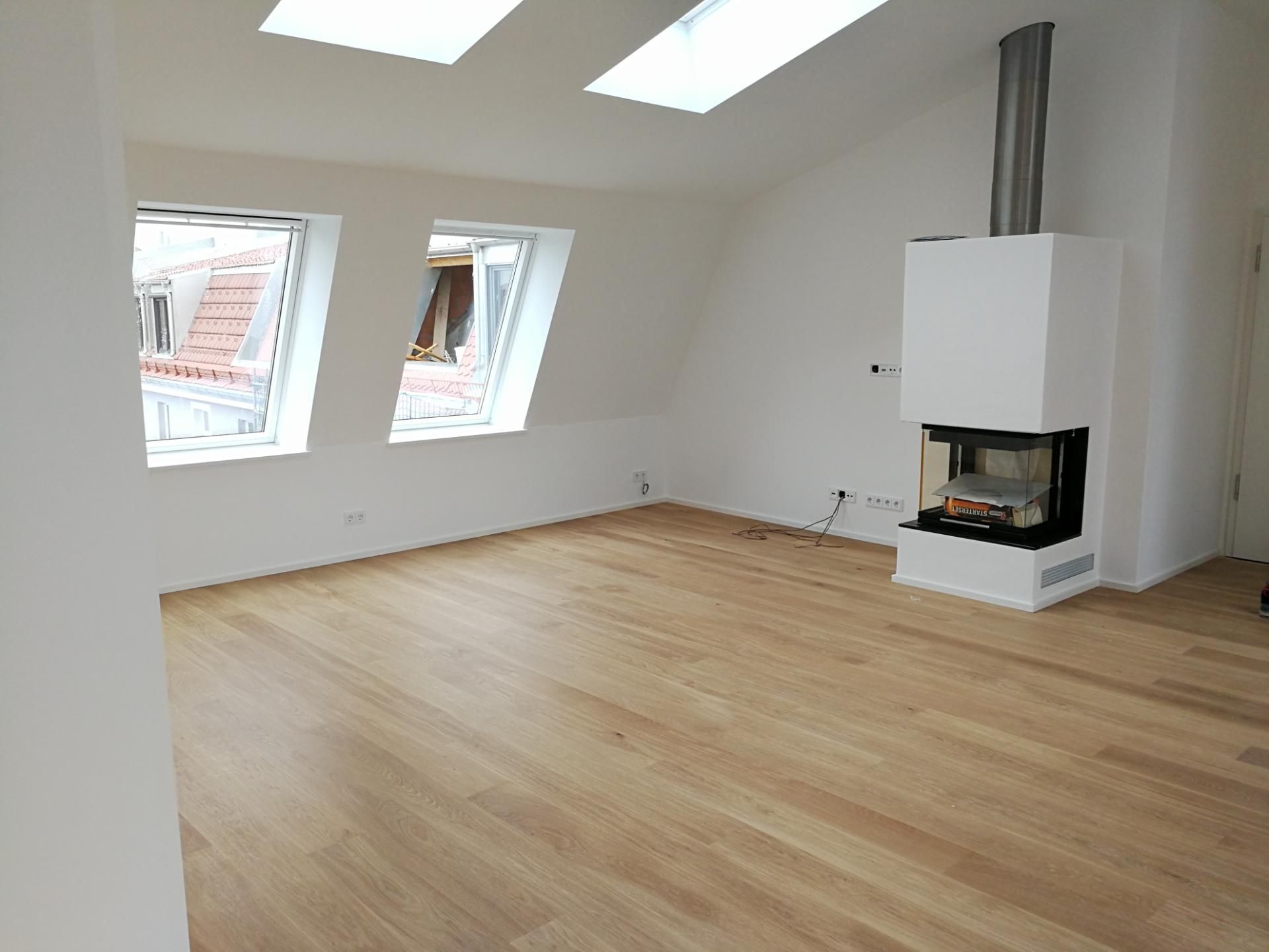 Heller Dachgeschossraum mit neuem Holzfußboden und Kaminofen in der Ecke.