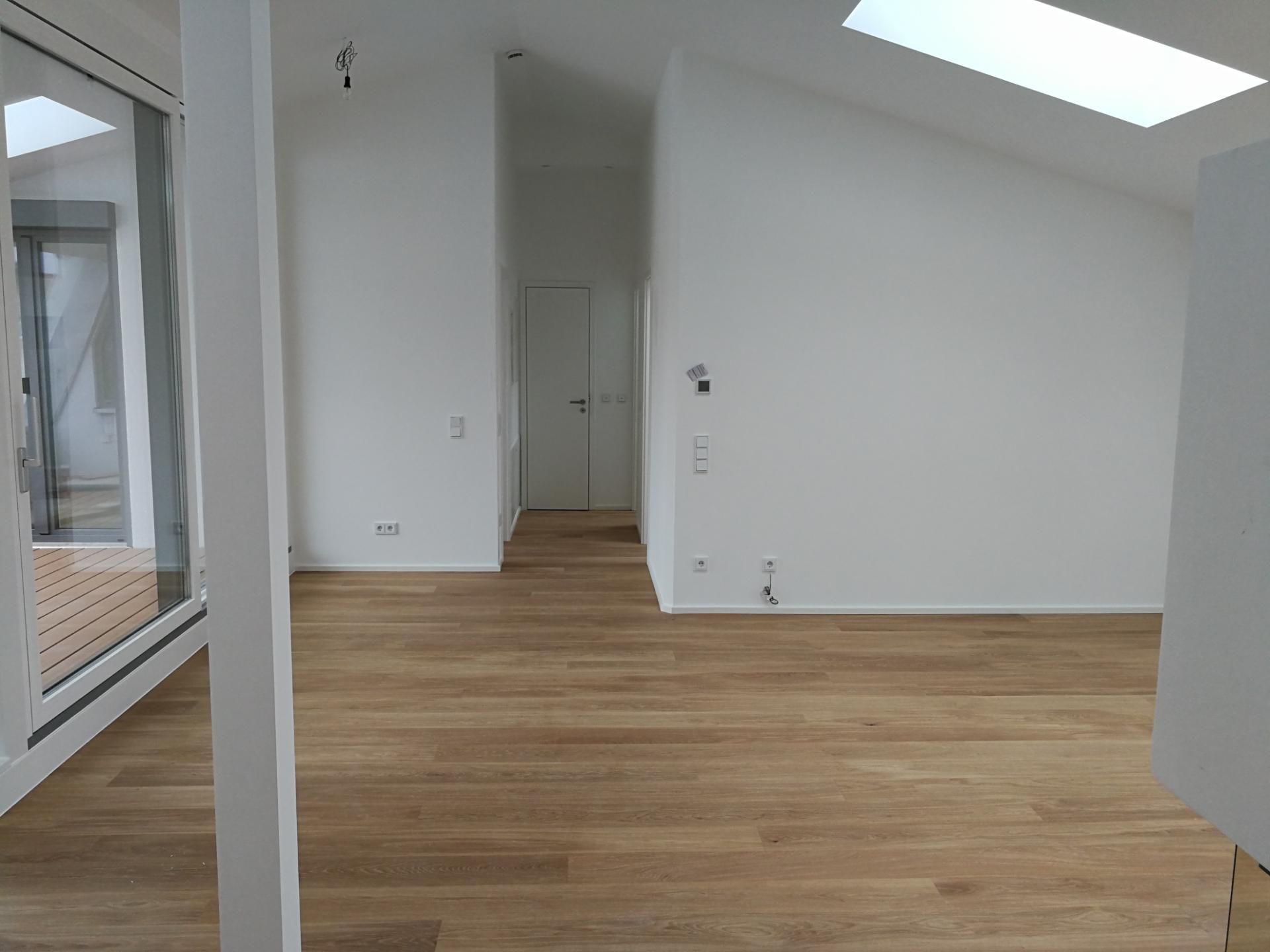 Heller Wohnraum mit Dachschräge und neu verlegtem Holzfußboden.