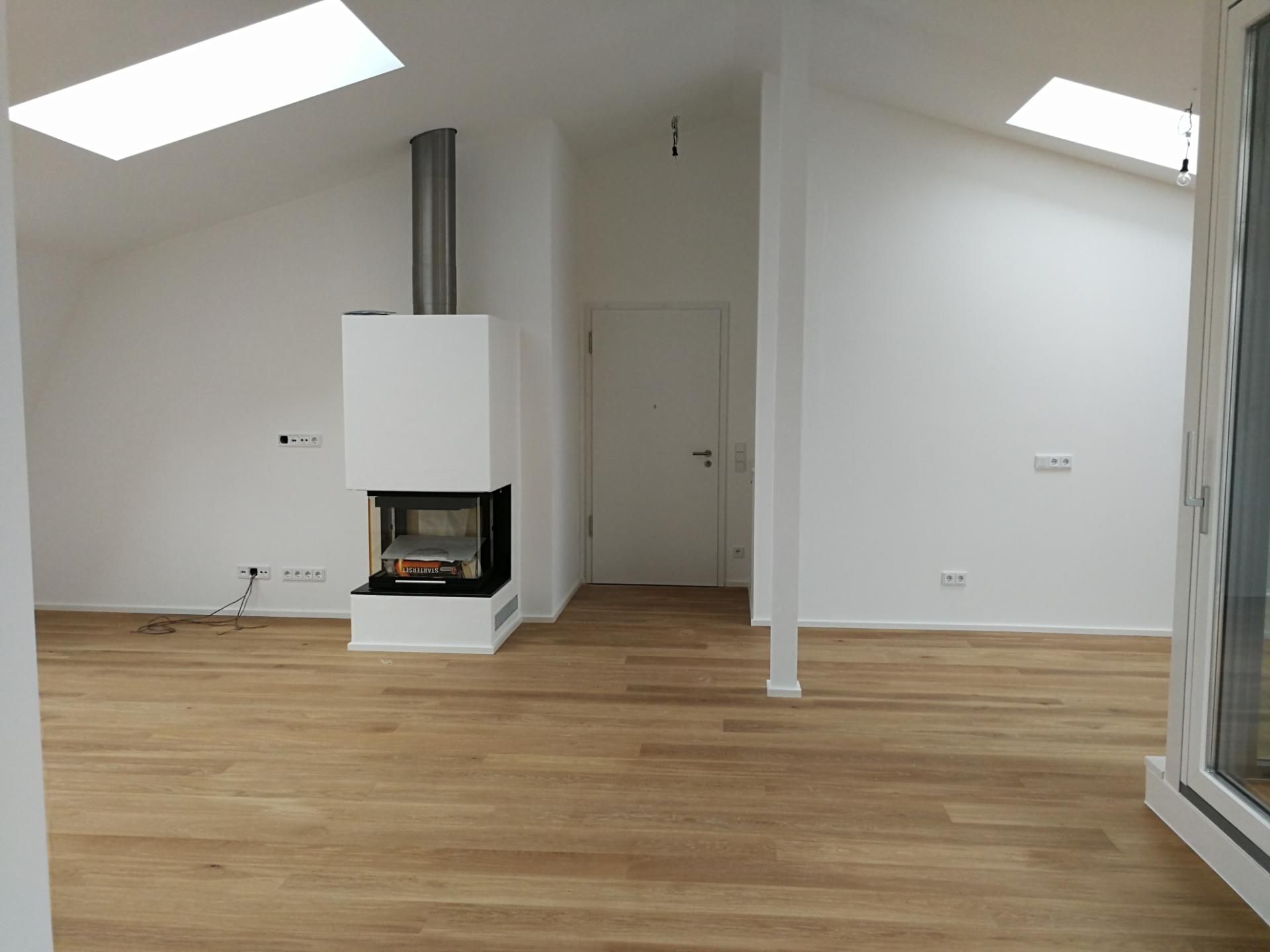 Leerer Raum mit Holzboden, weißem Kamin und zwei Dachfenstern in einer Dachschräge