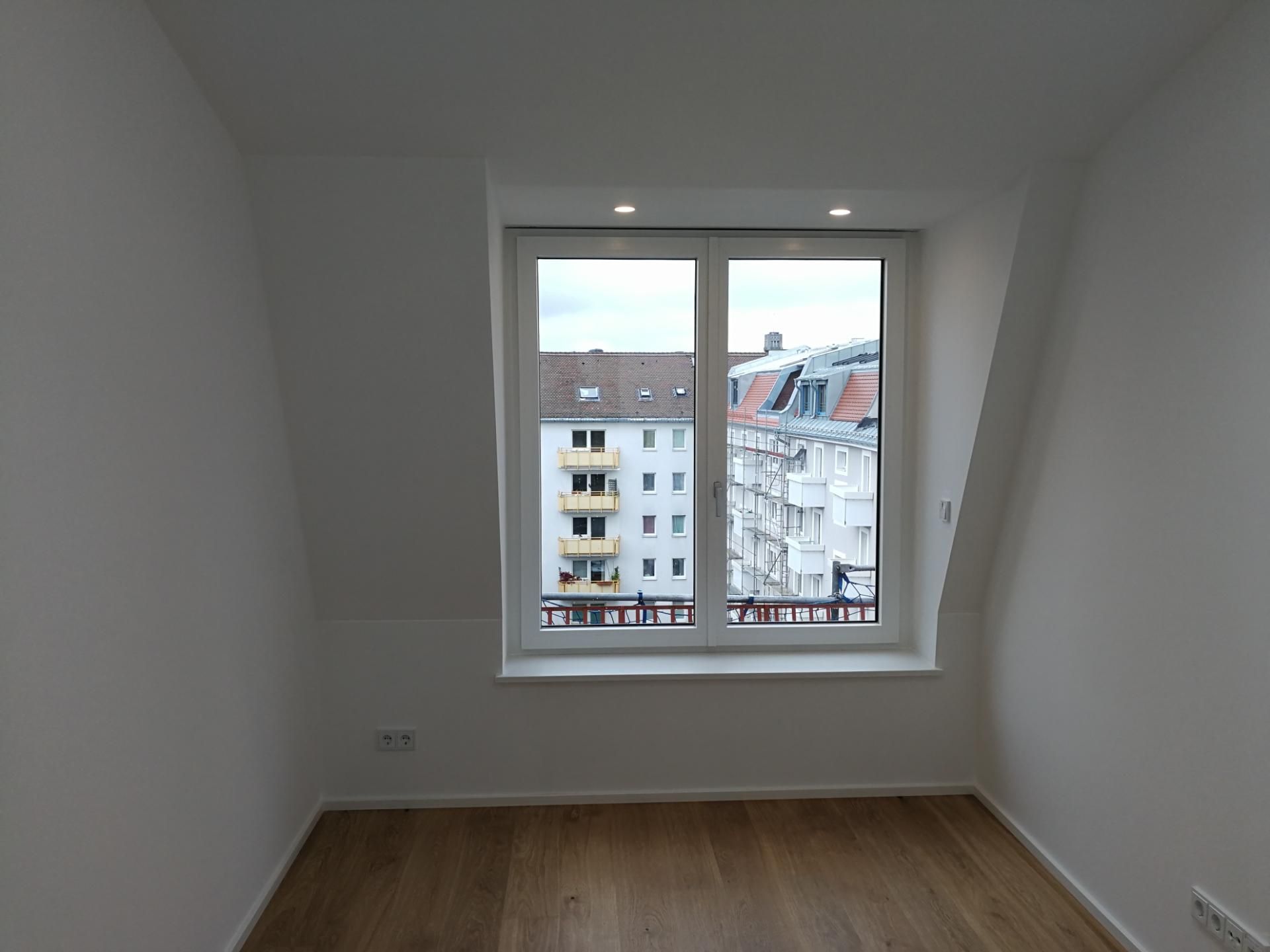 Kleines Dachzimmer mit Holzfußboden und Fenster mit Stadtblick.