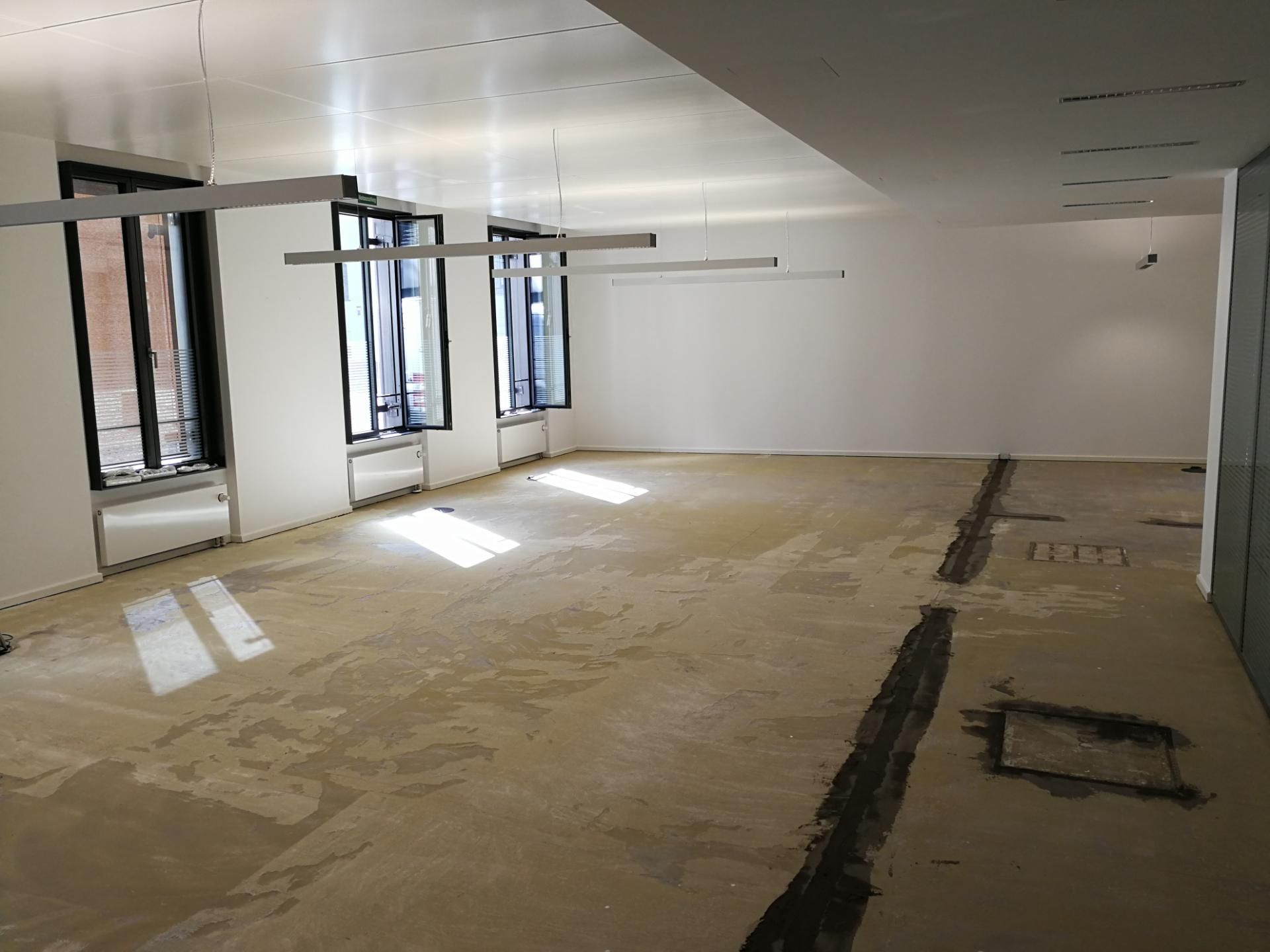 Großer Innenraum mit Bodenarbeiten im Gange, Fenster teilweise abgedeckt.