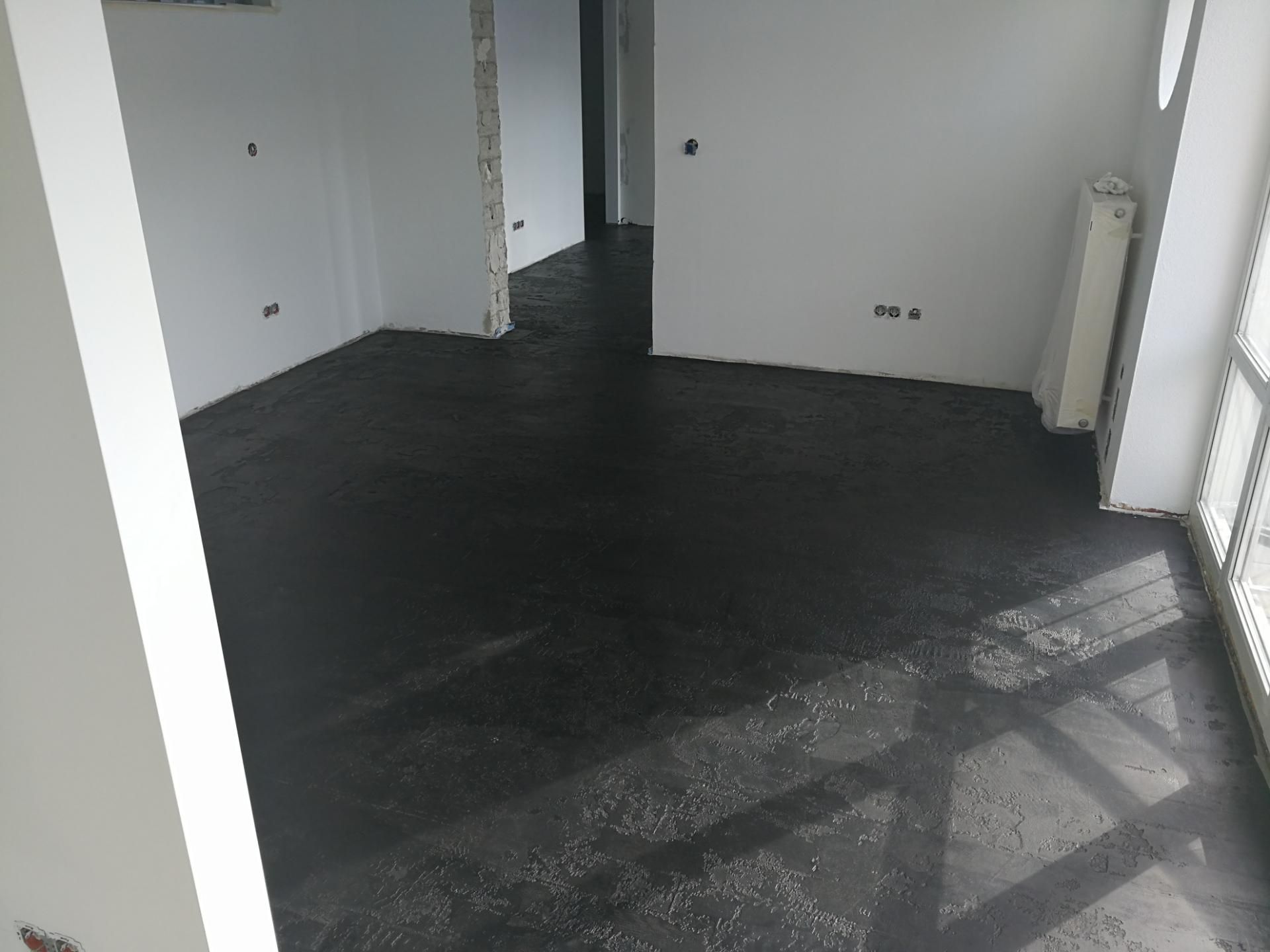 Teilweise renovierter Raum mit dunklem Bodenbelag und offenem Rohzustand.
