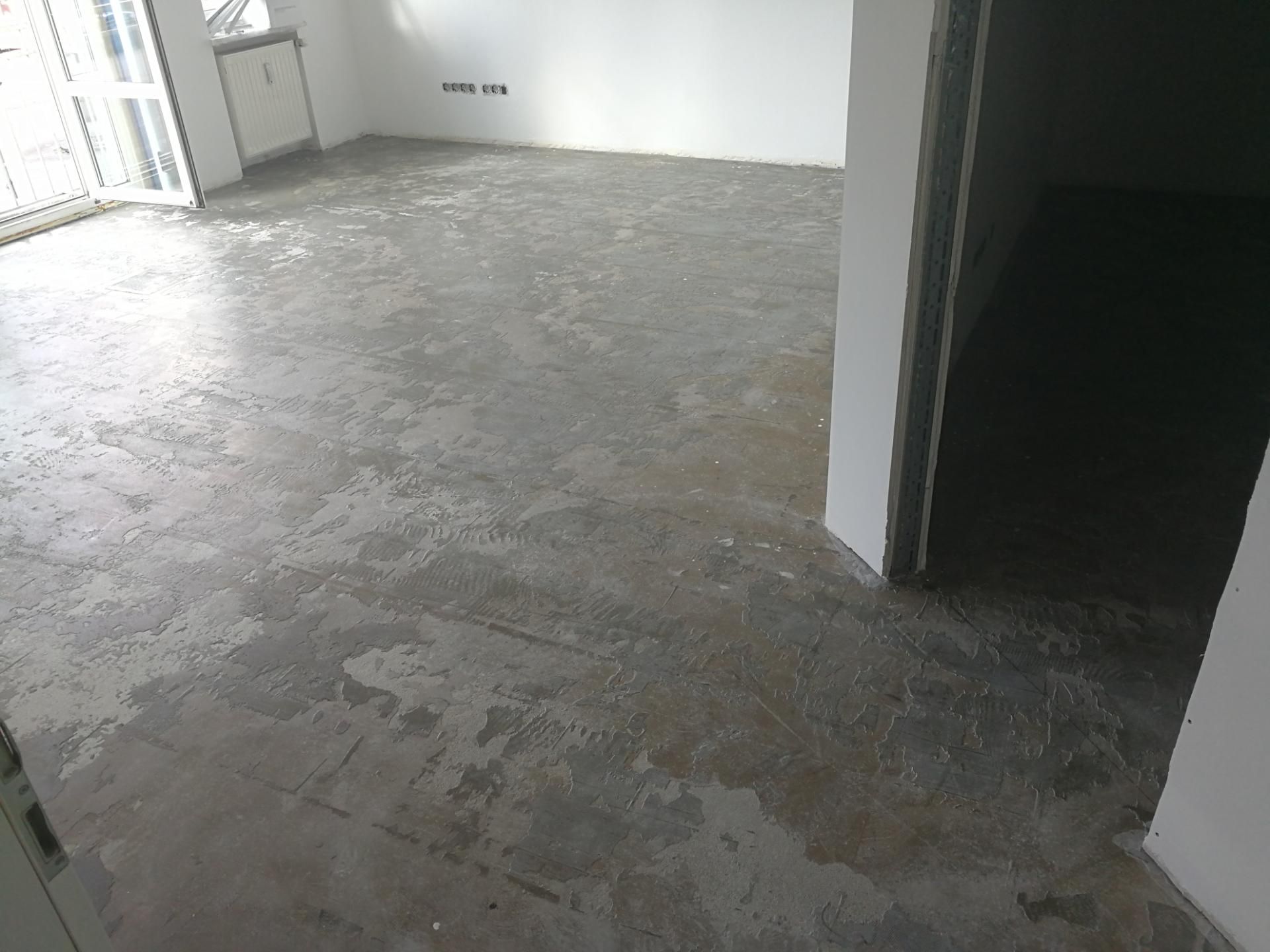 Raum mit dunklem, beschädigtem Untergrund, Bodenarbeiten noch im Gange.