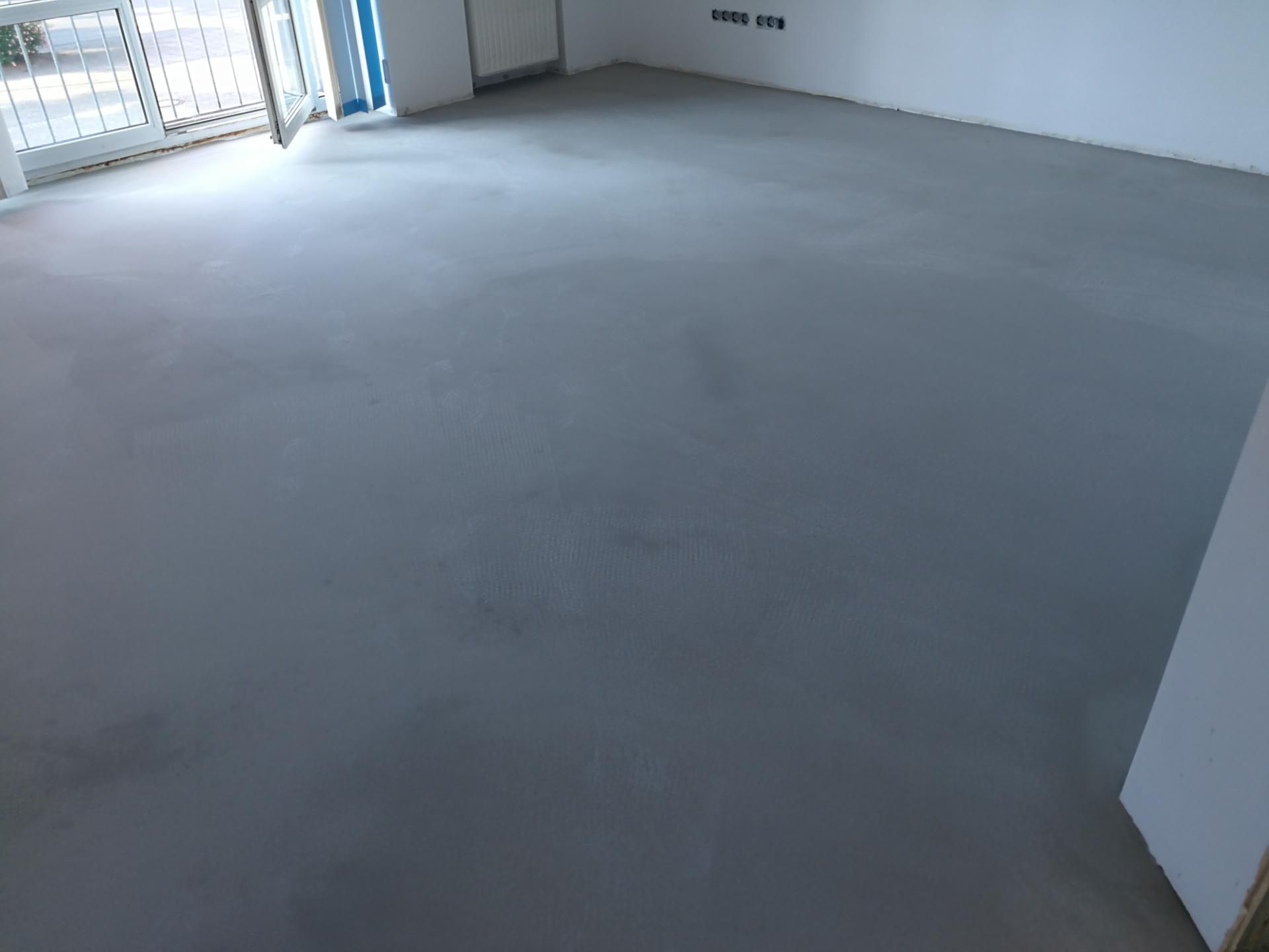 Glatt gespachtelter, dunkler Boden in einem leeren, hellen Raum.