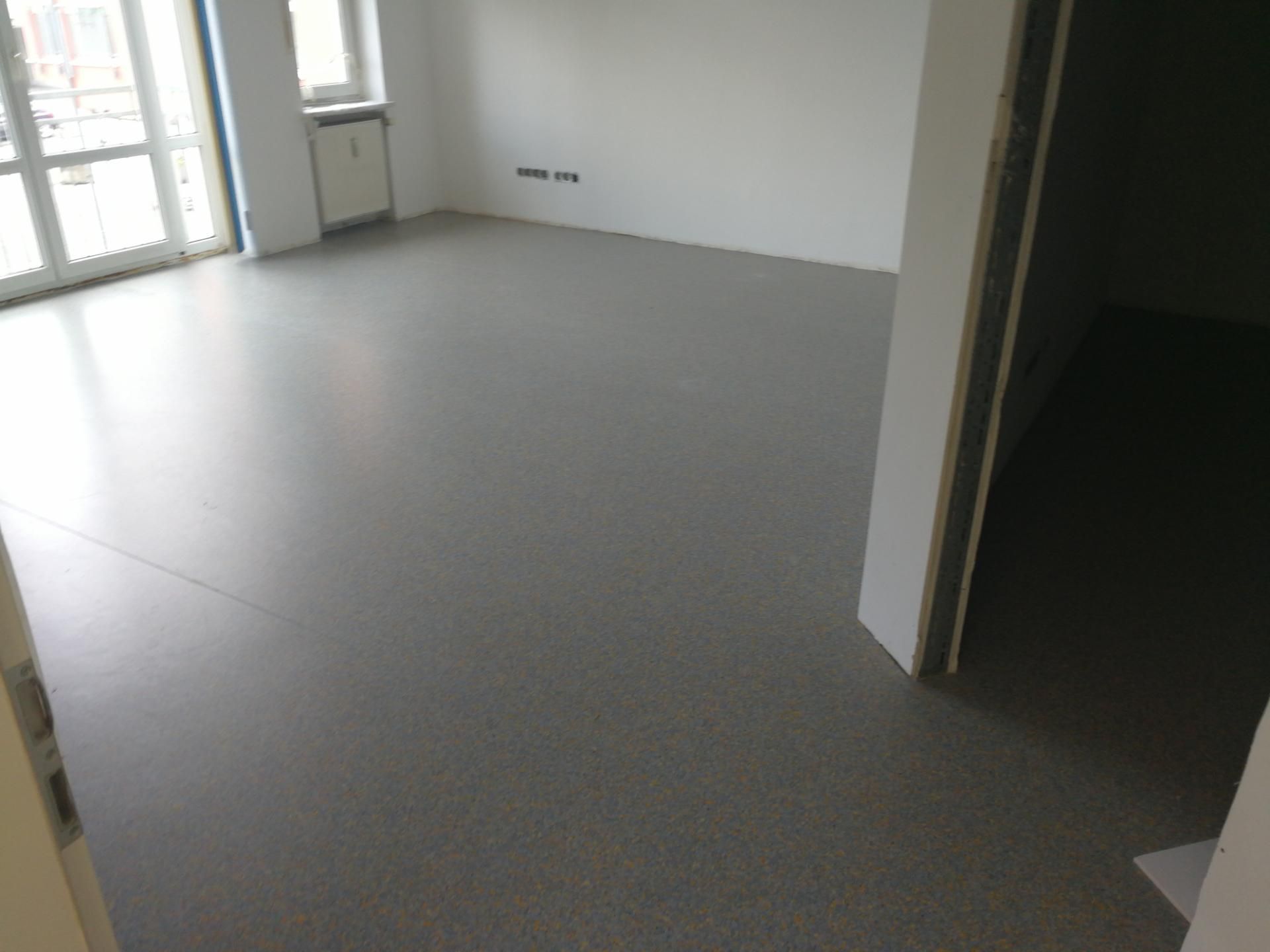 Neuer grauer Bodenbelag in einem hellen, leerstehenden Wohnraum.