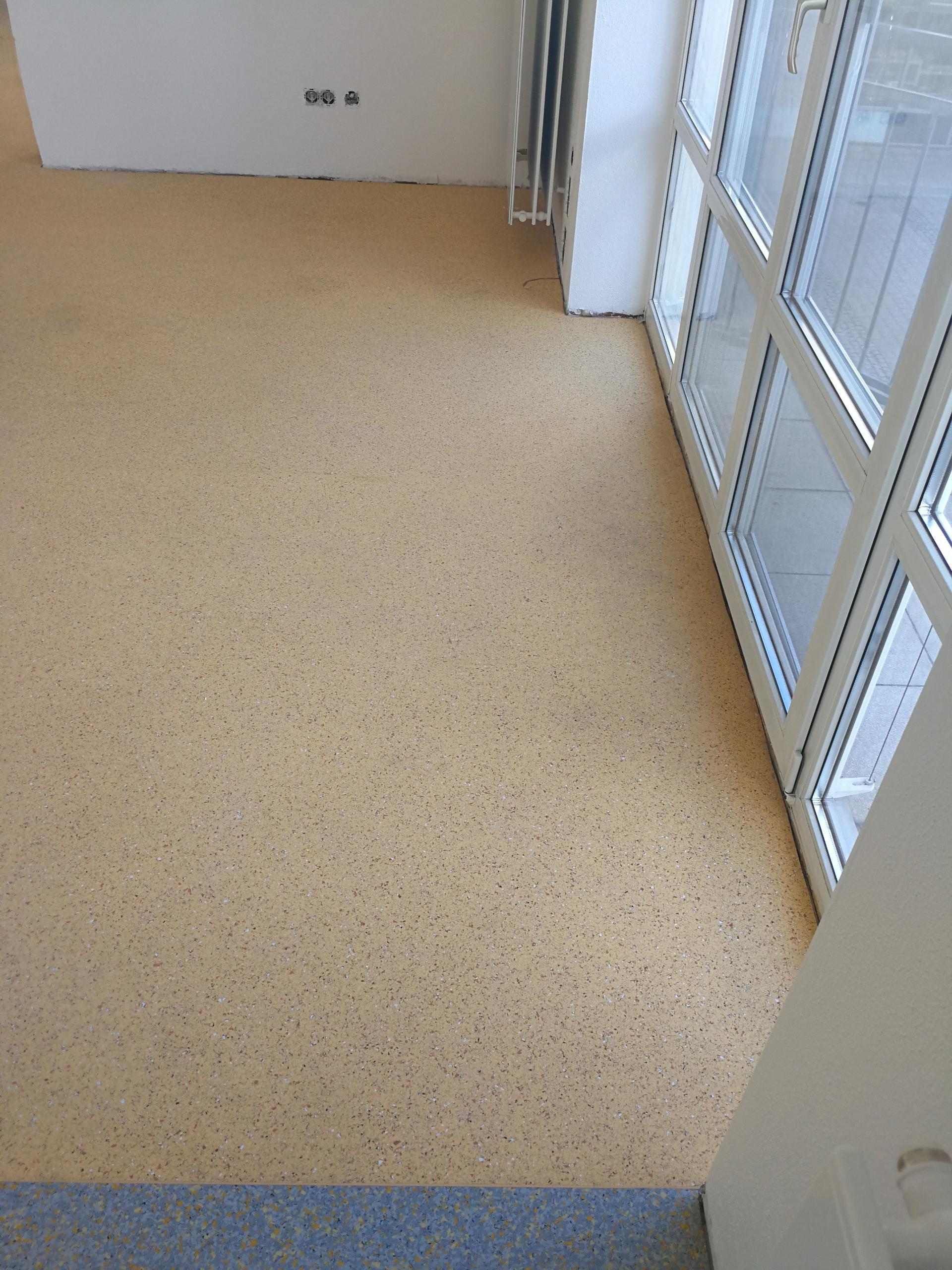 Nahaufnahme eines Raumes mit frisch verlegtem Korkboden und großen Fenstern.