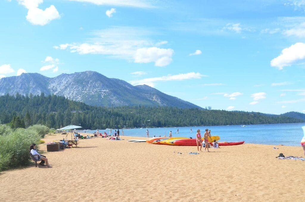 Crowds at Baldwin beach on a sunny day with kayaks on the sand and large mountain in background