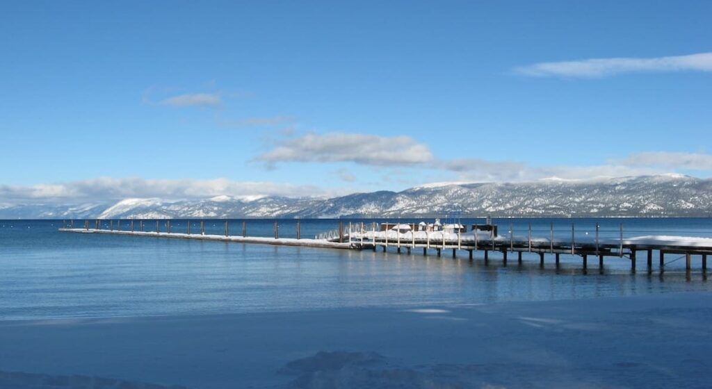 Long jetty at Camp Richardson with calm clue waters and snow-capped mountains in background