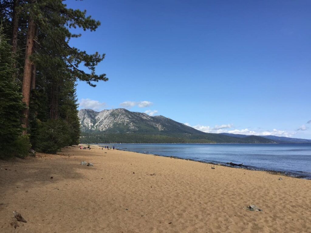 Empty beach at Kiva beach with tall green trees beside the sand and mountain in background