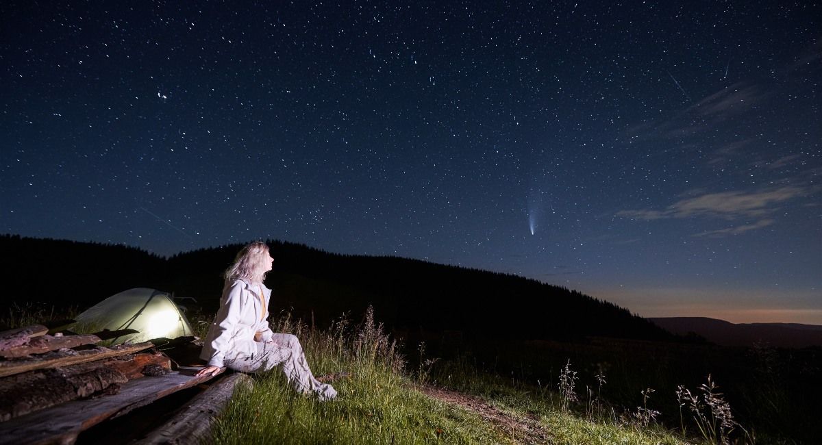 Young woman sitting in mountains with starry sky