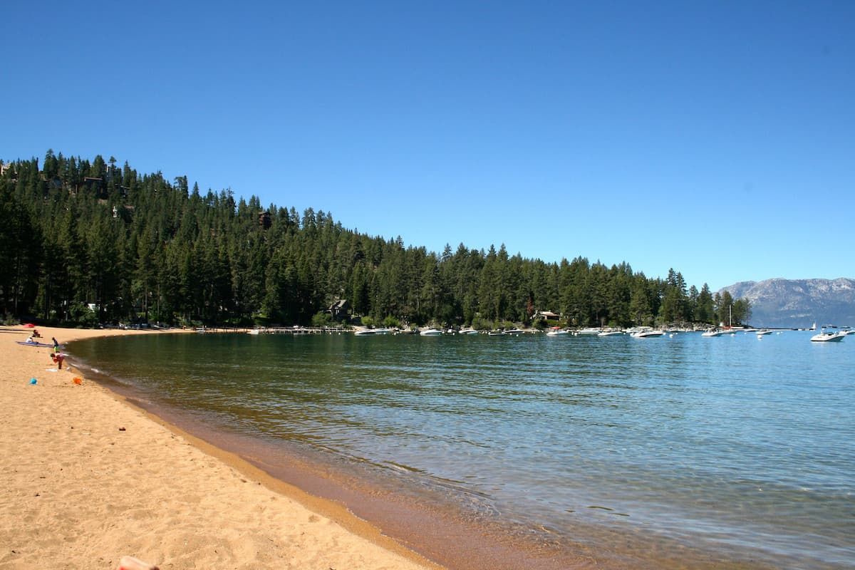 Sandy shoreline at Zephyr Cove with boats in the water and trees in background