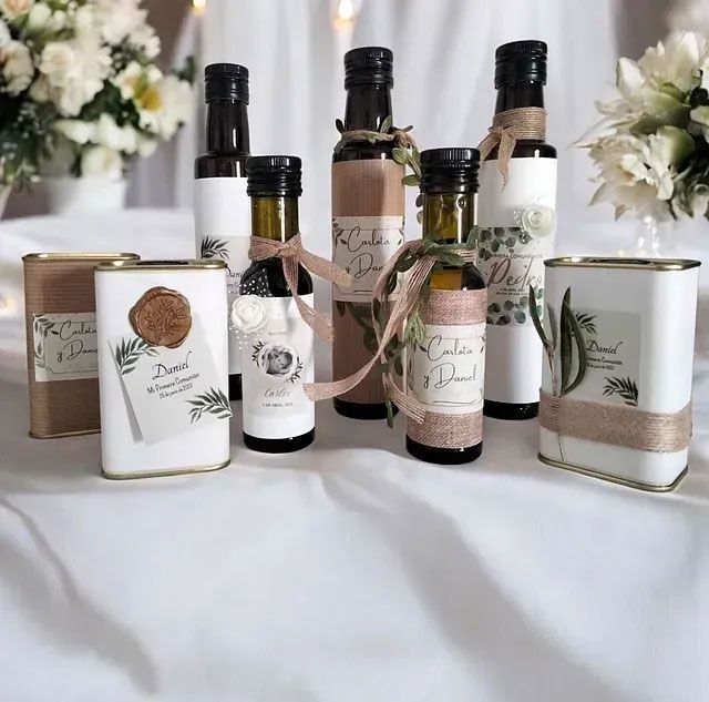 Botellas y latas de aceite de oliva con etiquetas decorativas y cintas sobre una superficie blanca.