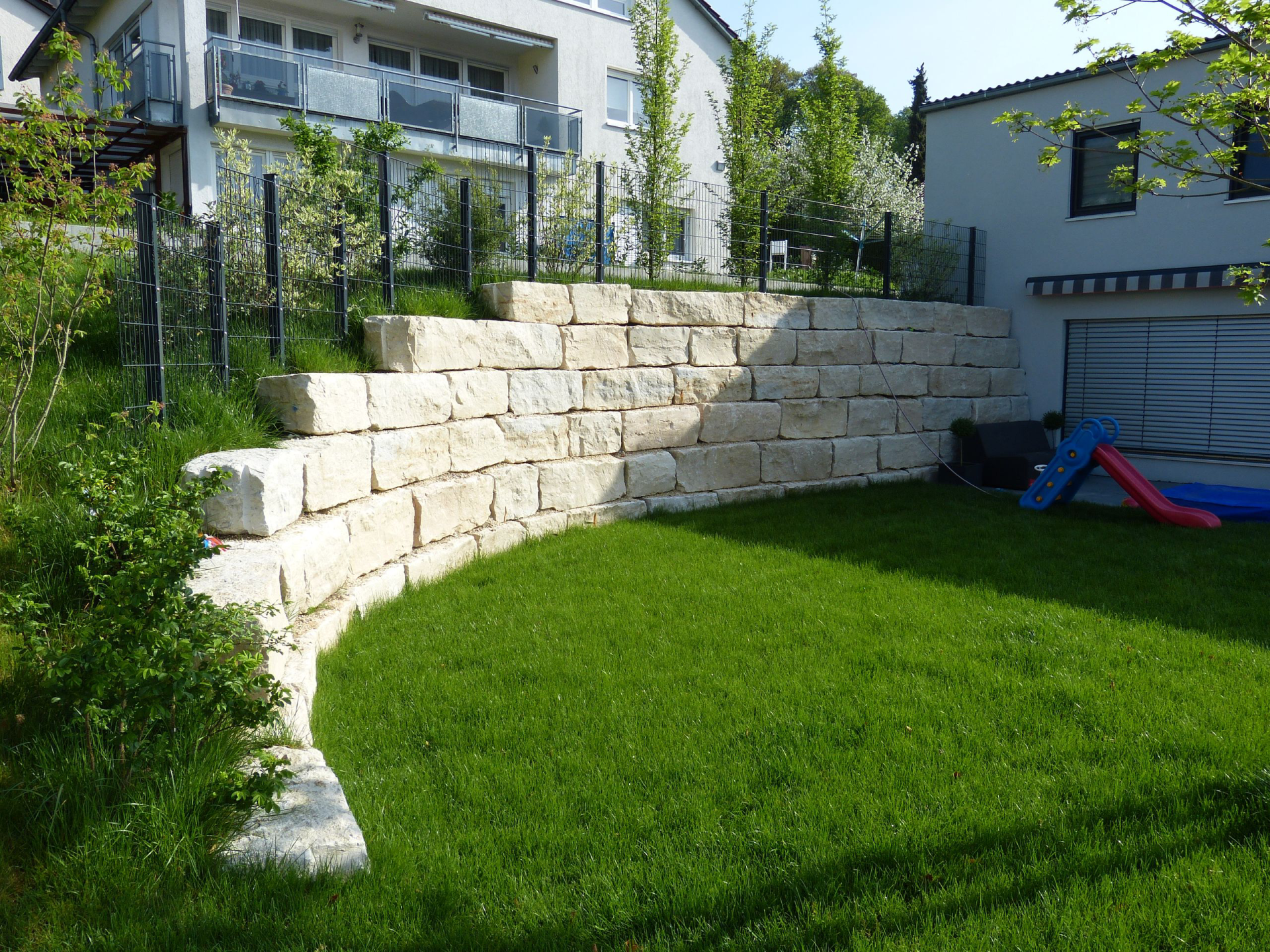 Eine große Steinmauer umgibt einen üppigen grünen Rasen vor einem Haus.
