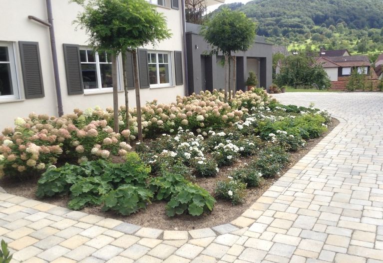 Eine gemauerte Auffahrt mit Blumen und Bäumen vor einem Haus