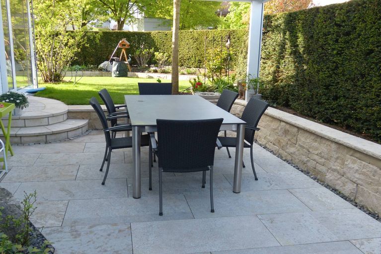 Ein Tisch und Stühle auf einer Terrasse in einem Garten.