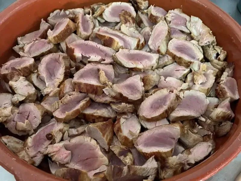 Un cuenco de terracota lleno de numerosas lonchas de solomillo de cerdo cocido, que deja ver el centro rosado.