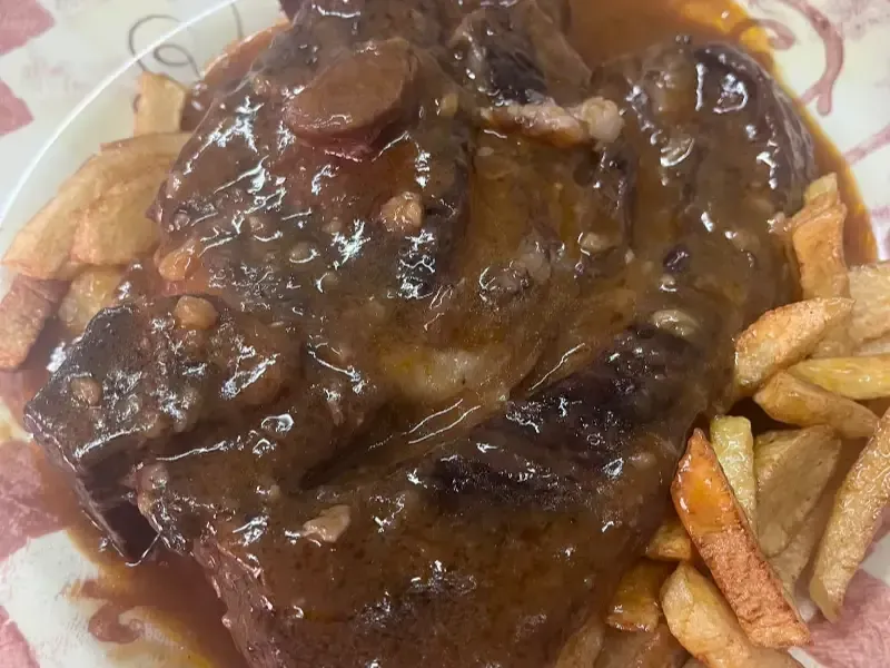 Un guiso de carne cubierto con salsa marrón, servido en un plato acompañado de patatas fritas doradas.