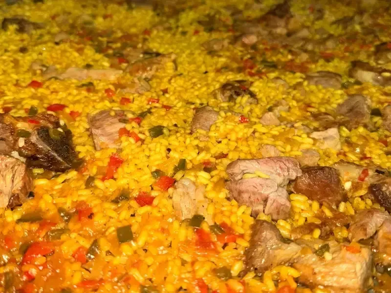 Primer plano de un sabroso plato de arroz amarillo mezclado con trozos de carne cocida, pimientos rojos y hierbas verdes.