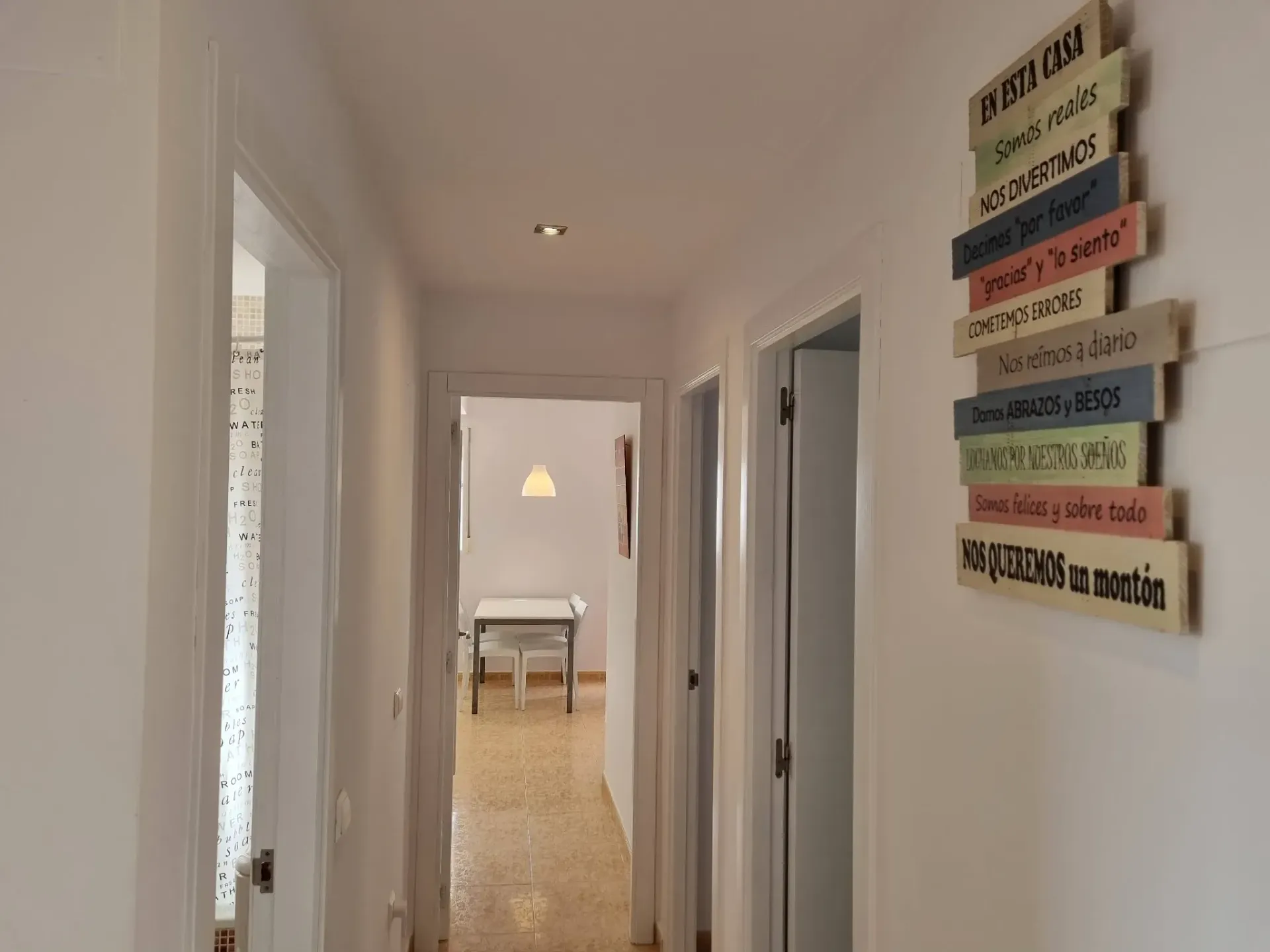 Pasillo con puertas y carteles decorativos de madera sobre pared blanca.