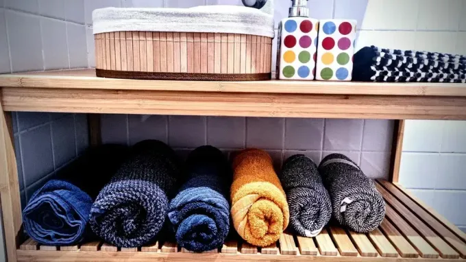 Toallas enrolladas y paños de baño ordenados cuidadosamente en estantes de madera en un baño o armario de ropa blanca.