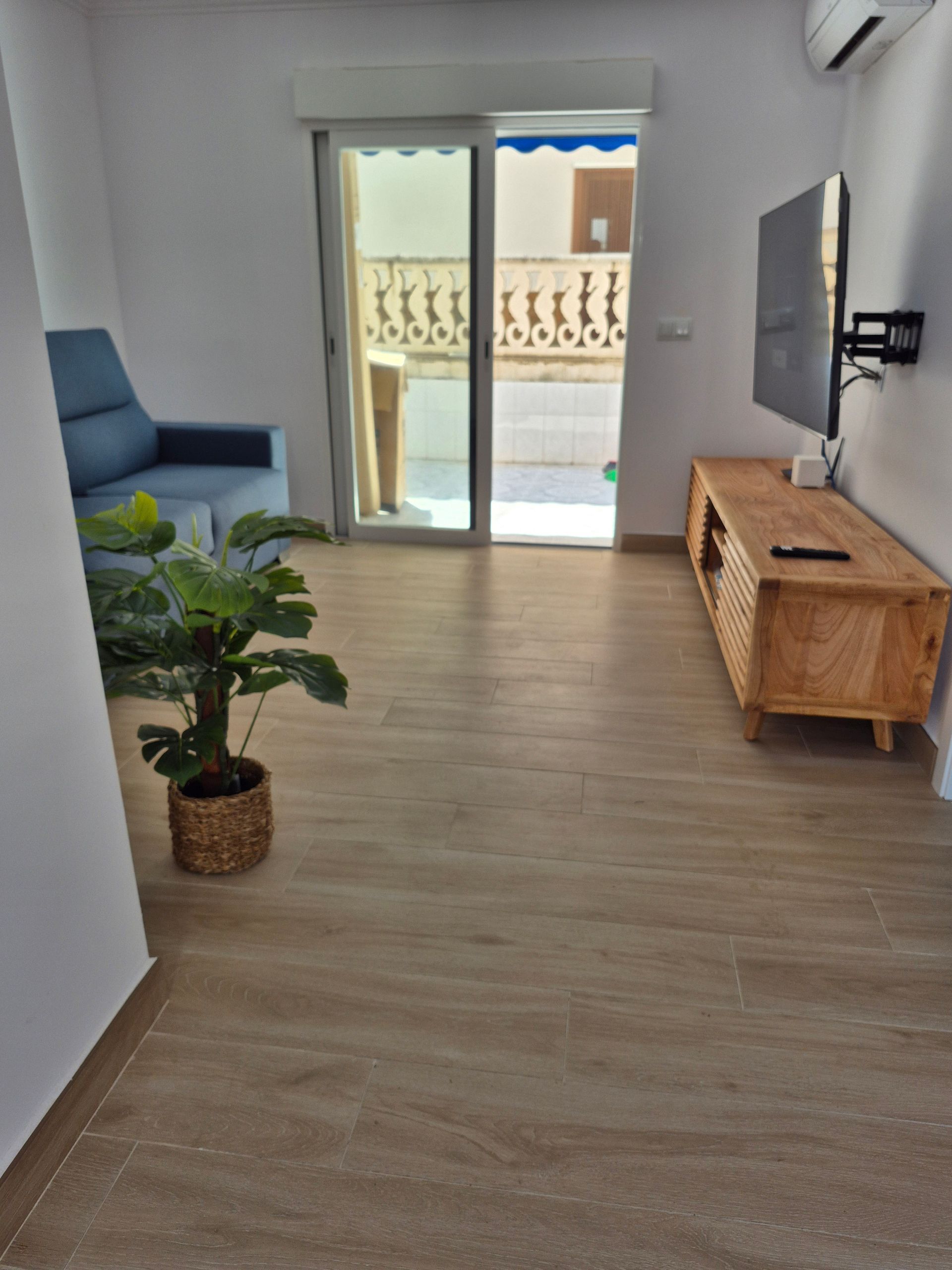 Sala de estar con sofá azul, mueble de TV de madera, una planta y puerta corrediza de vidrio.