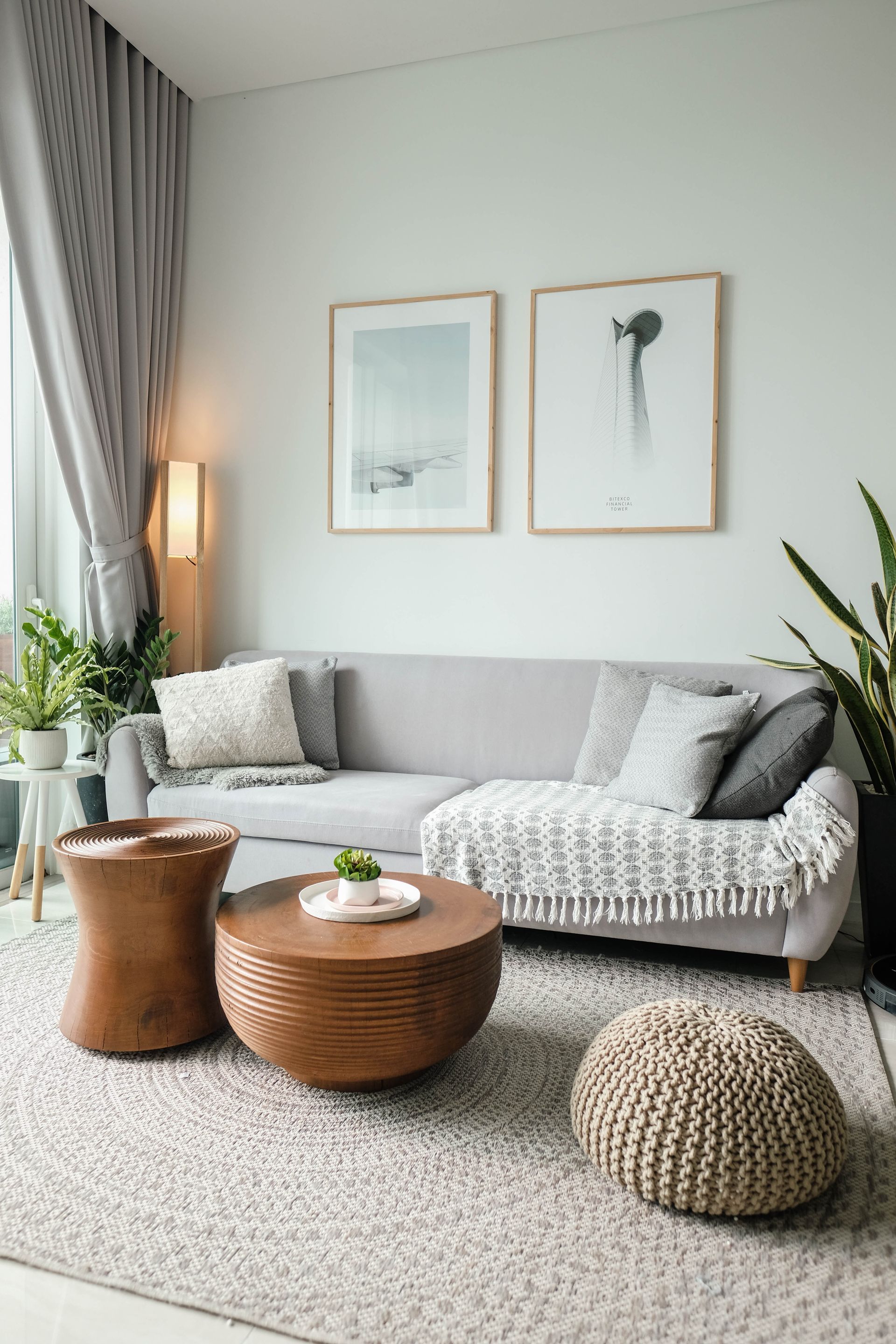 Living room with gray sofa, wooden coffee tables, plants, and art.