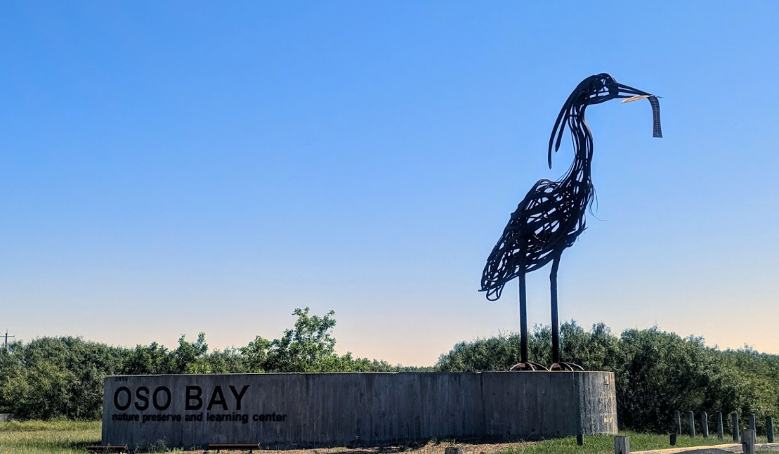 A statue of a bird standing next to a sign that says oso bay