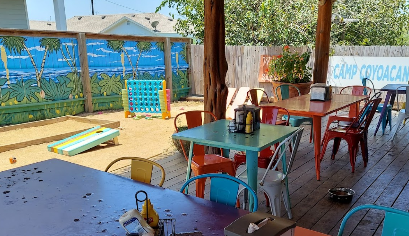 The patio at Lelo's Island Bar with tables and chairs and a sandbox in the background, and a dog bowl on the patio, food half eaten. 