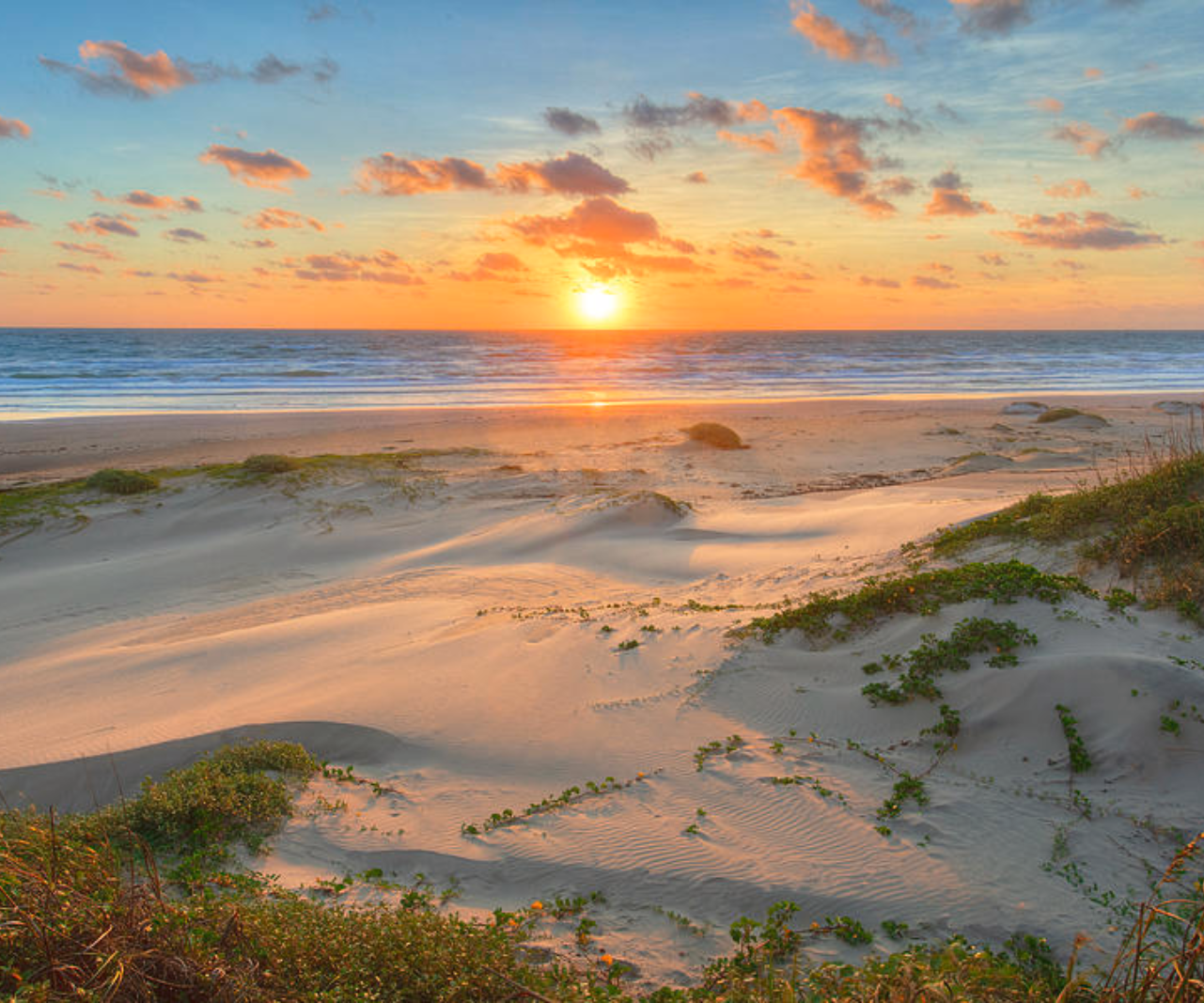 The sun is setting over the ocean on a sandy beach in Padre Island, Texas