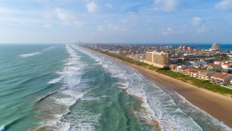 An aerial view of a beach with waves crashing against it and a city in the background.