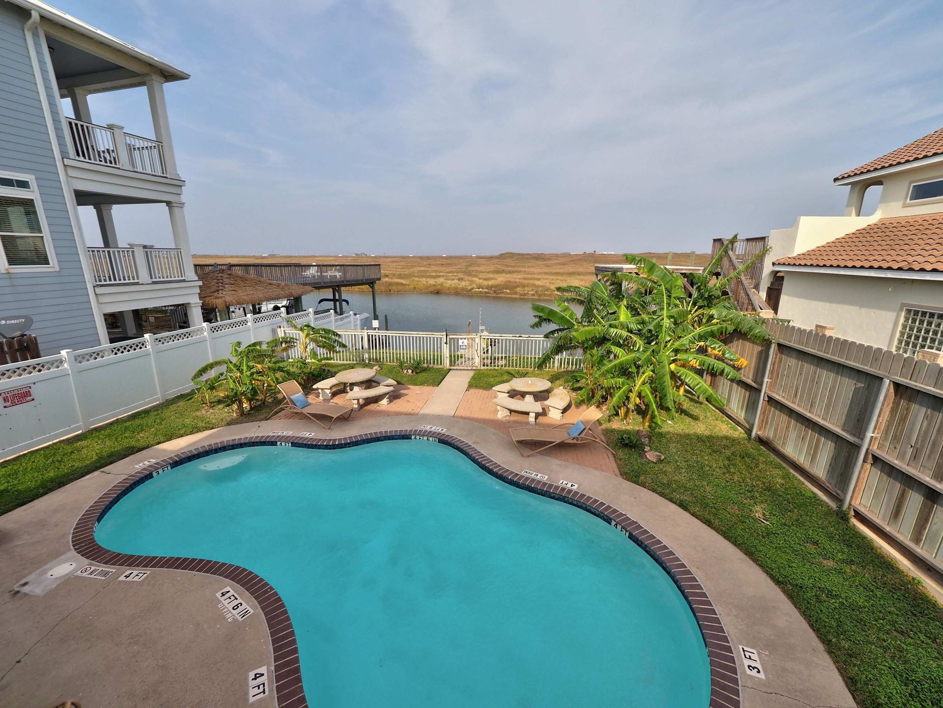 Resort pool with turquoise water, lounge chairs, palm trees, and ocean view at sunset