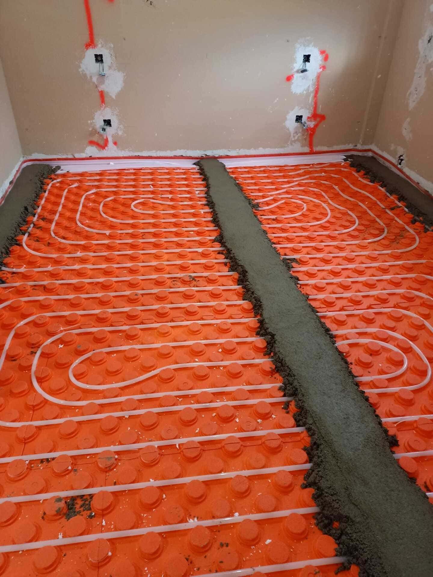 Tuberías rojas de calefacción por suelo radiante instaladas sobre material aislante, parcialmente cubiertas por una franja central de hormigón.
