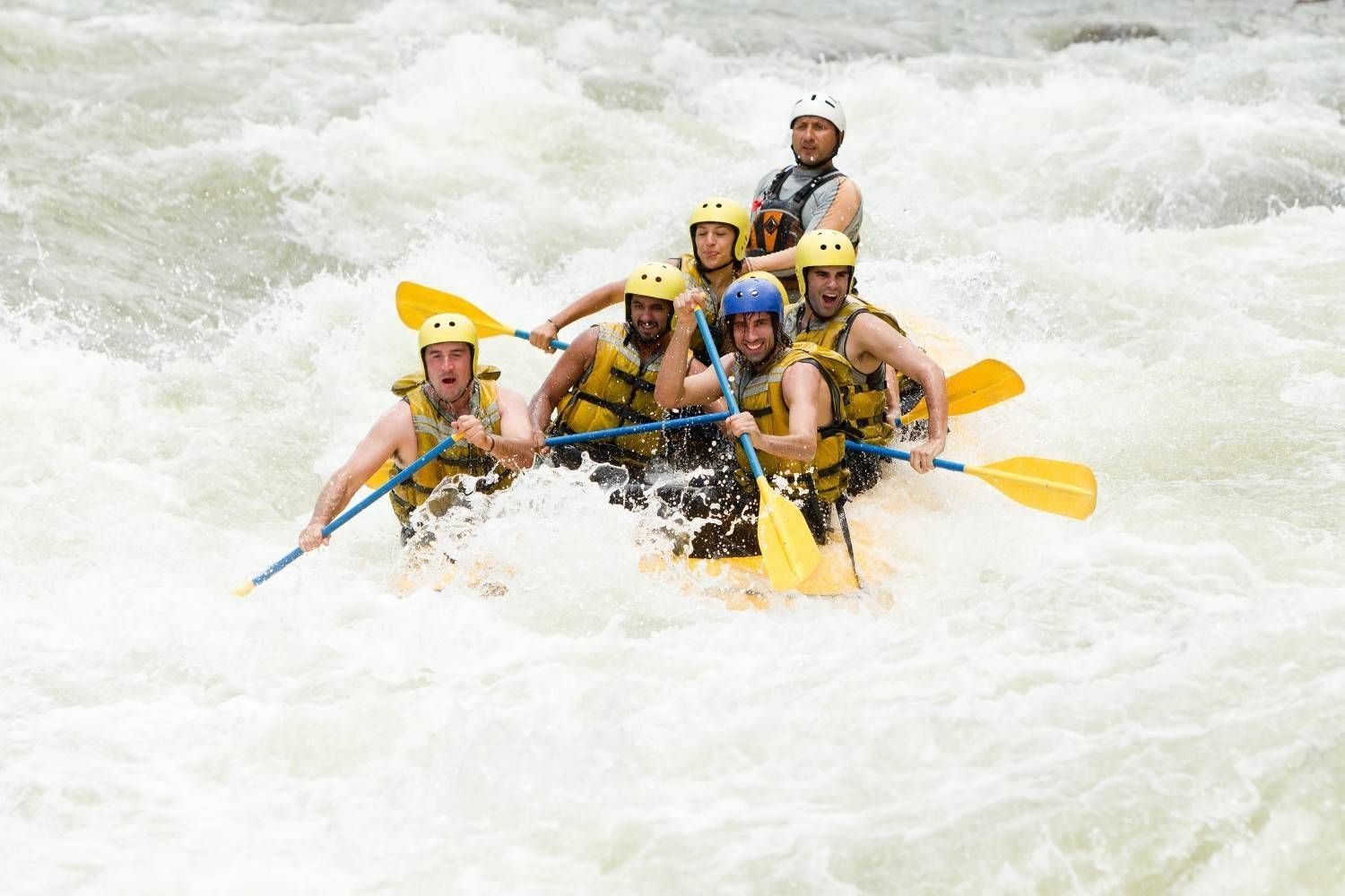 Un grupo de personas con chalecos salvavidas y cascos practicando rafting en aguas bravas a través de rápidos turbulentos.