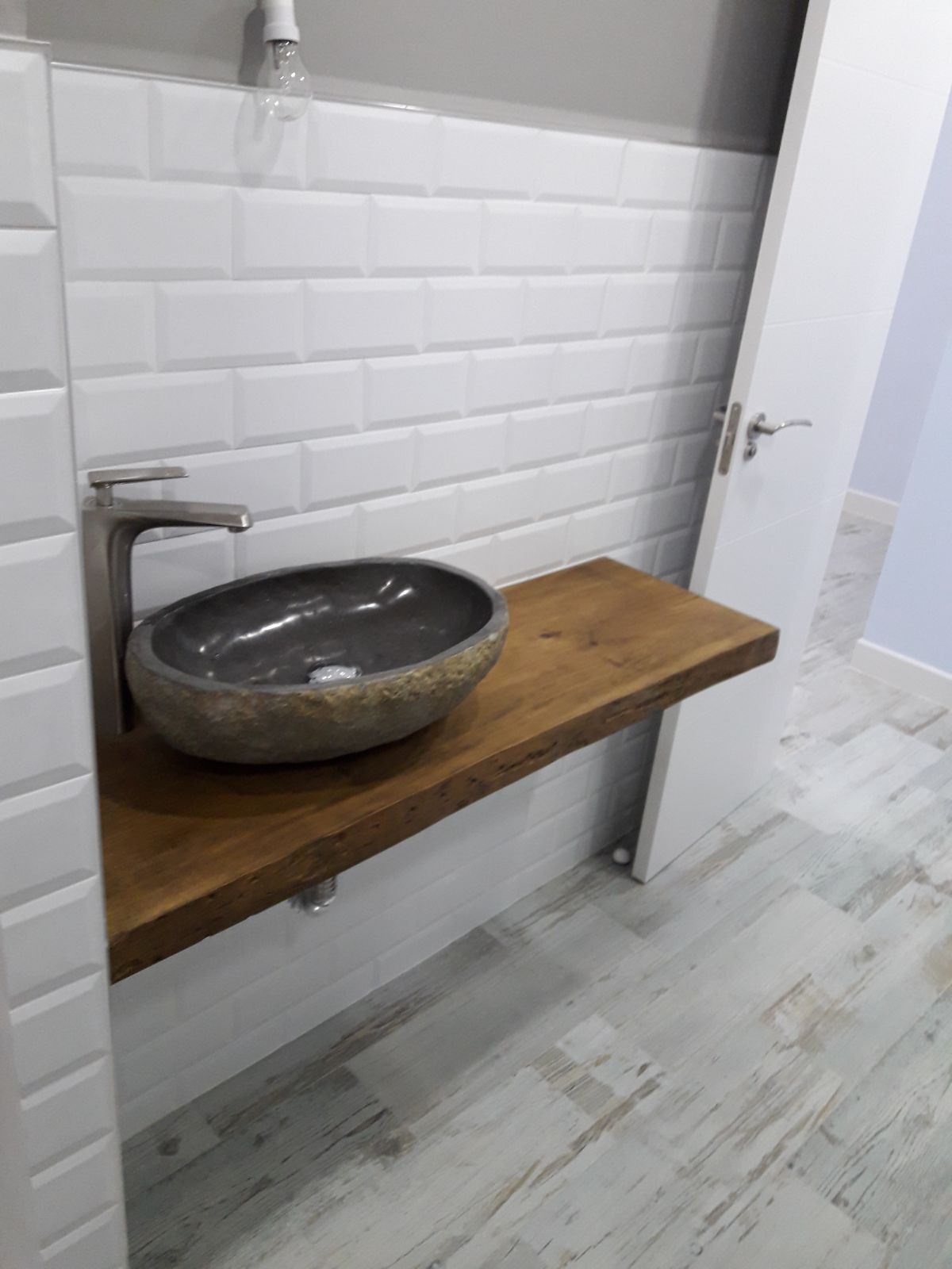 Baño con lavabo de piedra gris sobre estante flotante de madera oscura, pared de azulejos del metro y piso de madera clara.