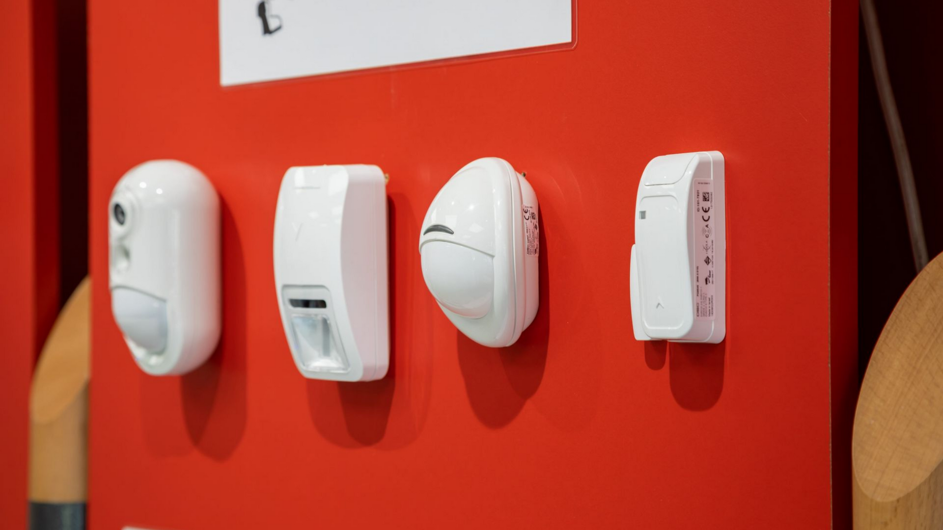 Quatre capteurs de sécurité blancs fixés sur un mur rouge.