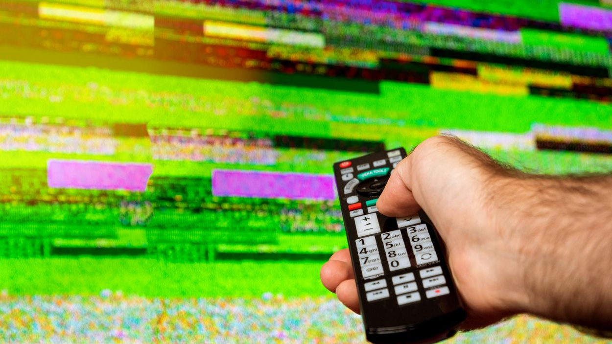 Main tenant une télécommande pointée vers un écran de télévision présentant des parasites.