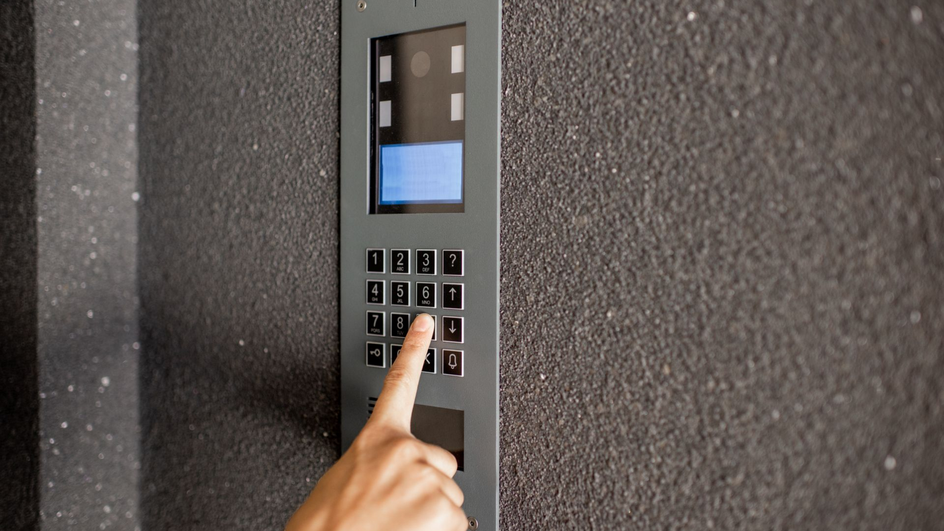 Une main appuie sur le chiffre 3 d'un clavier à écran d'un interphone de résidence fixé sur un mur.