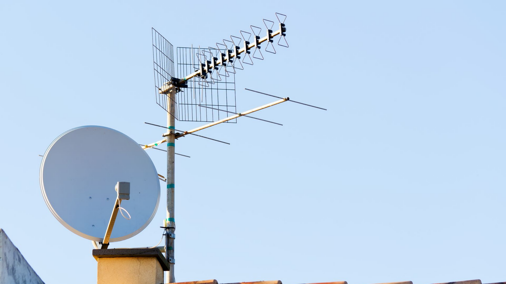 Toit avec une antenne parabolique et une antenne de télévision sur fond de ciel bleu dégagé.