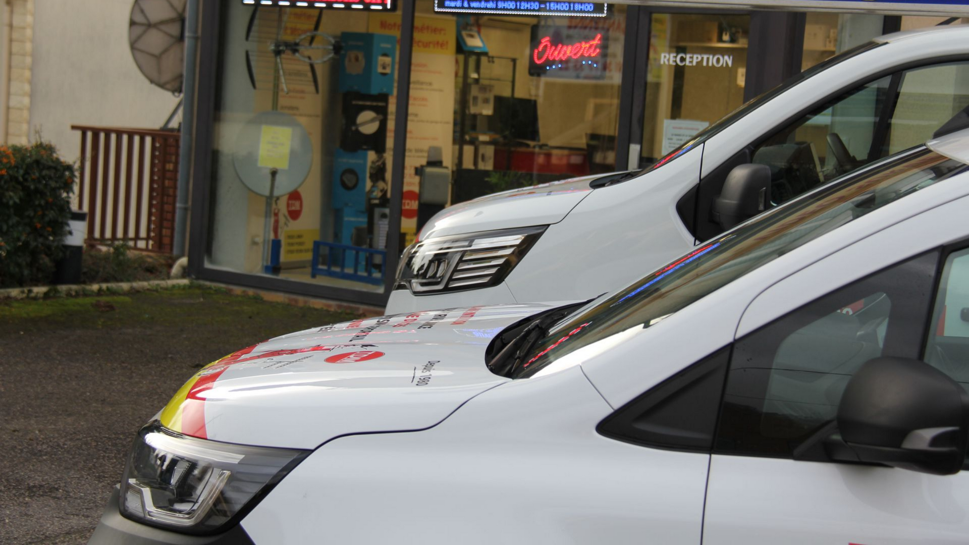 Une camionnette blanche est stationnée devant un magasin arborant des panneaux de sécurité.