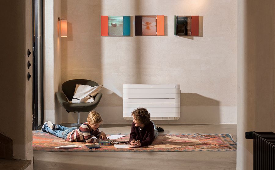 Deux enfants jouent sur un tapis dans une pièce confortable équipée d'un radiateur mural, d'une chaise et de décorations murales colorées.