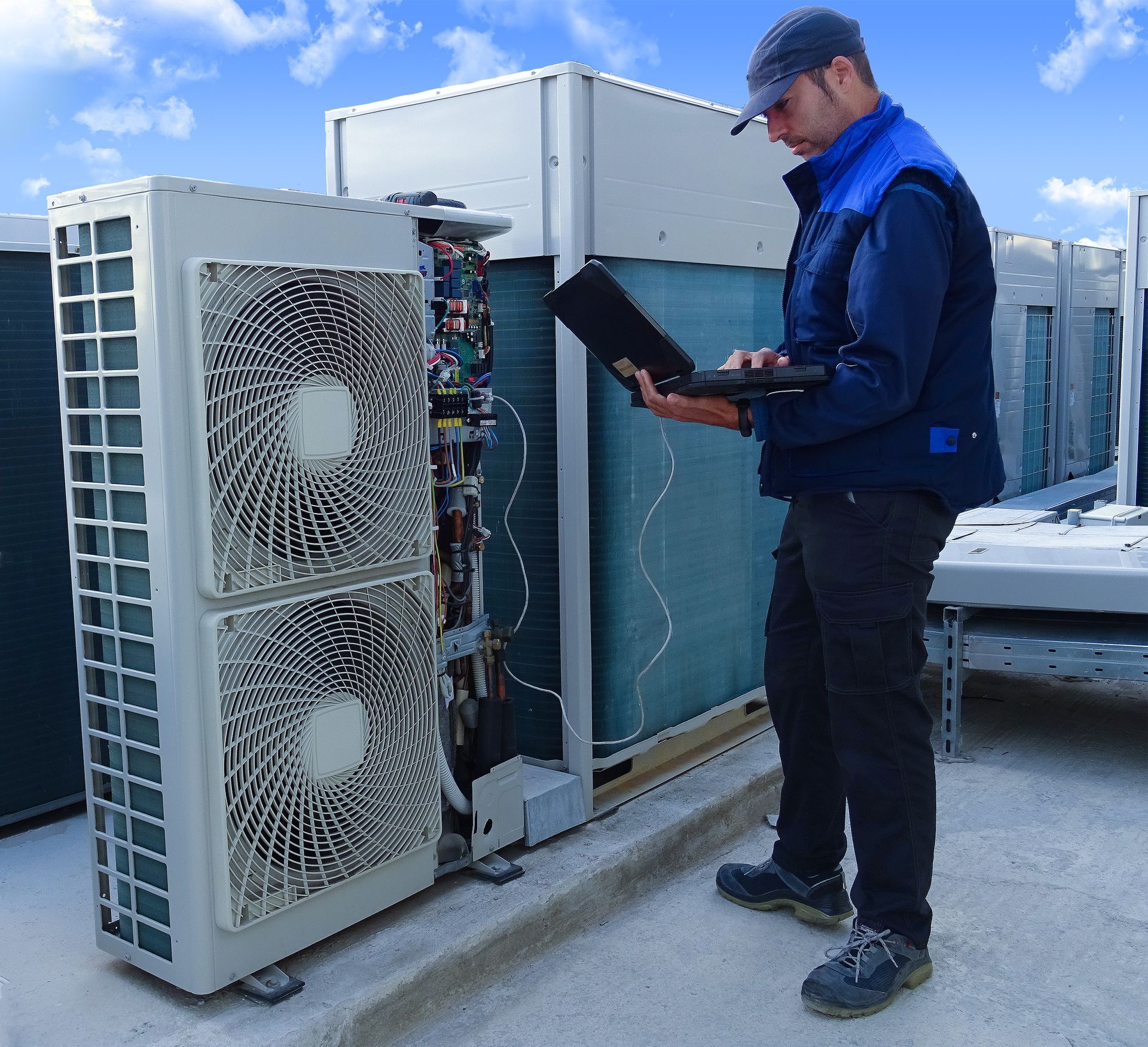 Un technicien utilise un ordinateur portable pour inspecter les unités de climatisation sur le toit par une journée ensoleillée.