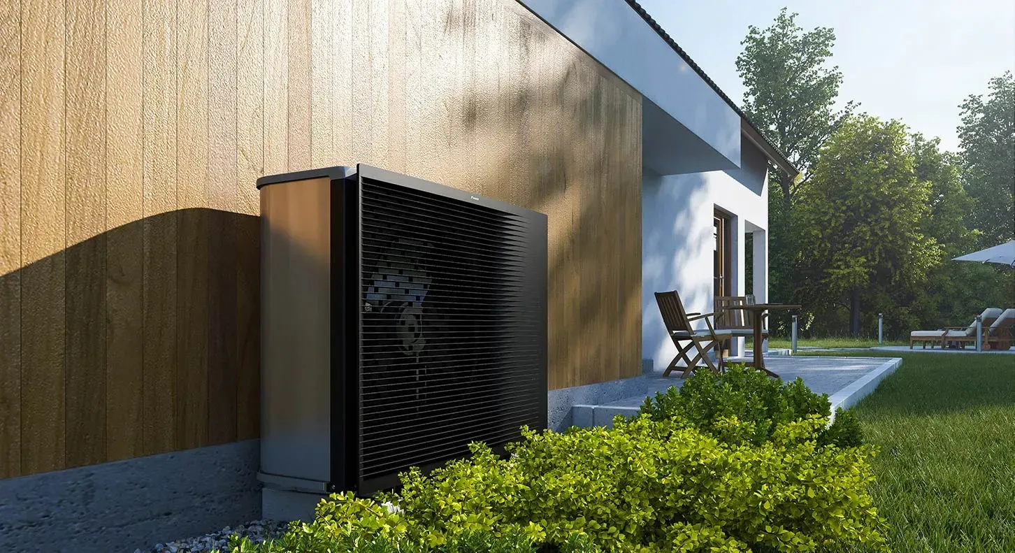 Extérieur d'une maison moderne avec un système de ventilation noir, des arbustes verts et des chaises de patio au soleil