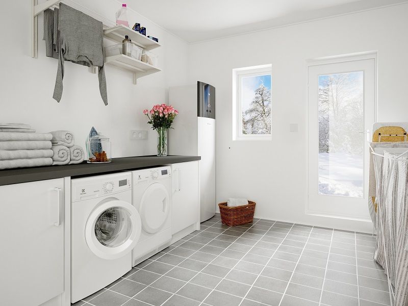 Buanderie lumineuse avec lave-linge, sèche-linge, placards blancs, sol gris et porte vitrée.