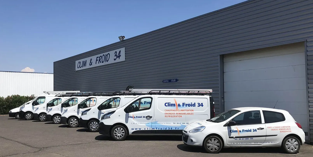 Des fourgonnettes de service blanches sont garées devant un entrepôt gris doté d'une grande porte de garage.
