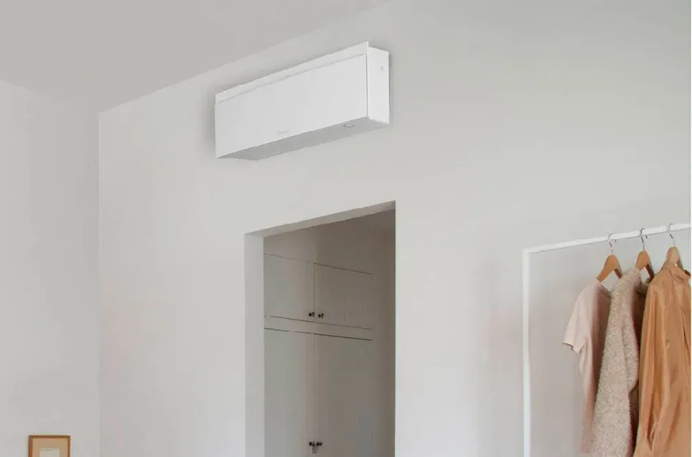 Climatiseur mural blanc au-dessus d'une porte ouverte dans une pièce lumineuse avec un portant à vêtements.