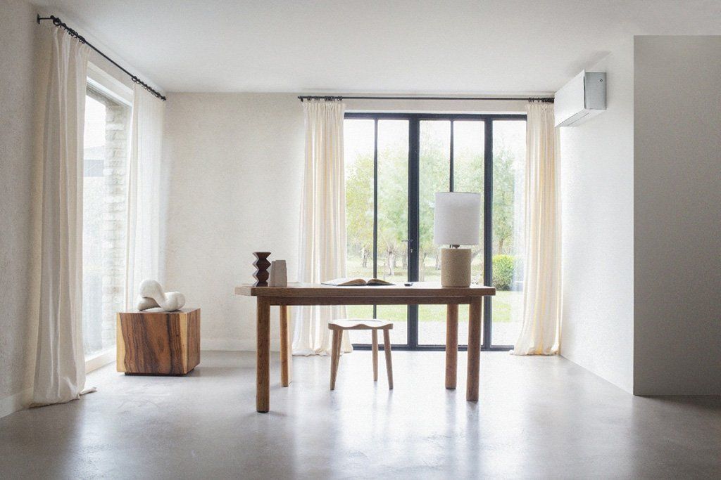 Pièce lumineuse et minimaliste avec table en bois, tabouret, lampadaire et grandes fenêtres avec rideaux.