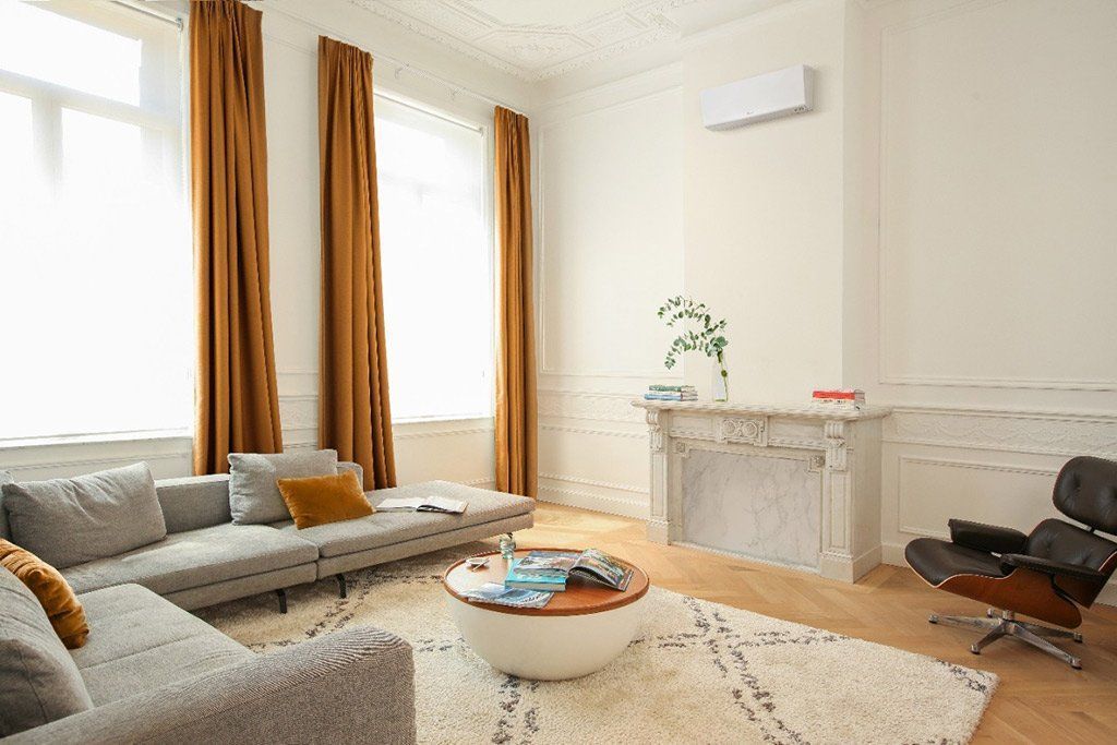 Salon moderne et lumineux avec canapés gris, grandes fenêtres, table basse ronde et cheminée blanche.